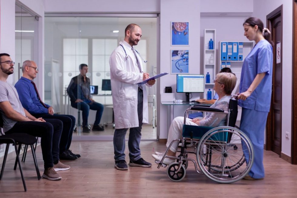 doctor-checking-diagnosis-paralyzed-disabled-senior-woman-wheelchair-sitting-reception-room